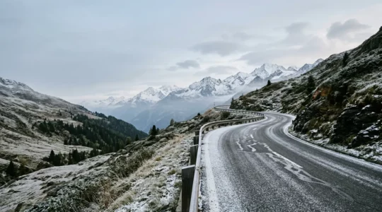 Véhicule sur route alpine suisse enneigée illustrant la transition entre saisons et l'importance de l'équipement hivernal