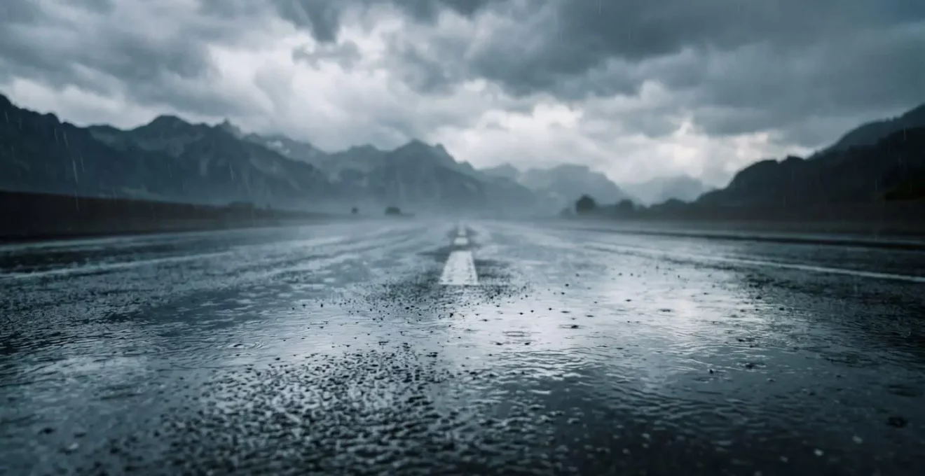 Vue environnementale d'une route suisse sous forte pluie avec flaques d'eau importantes, illustrant les conditions propices à l'aquaplaning