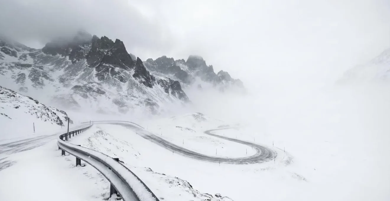 Vue grand angle d'un col alpin suisse sous conditions hivernales sévères avec signalisation de fermeture, illustrant les dangers invisibles