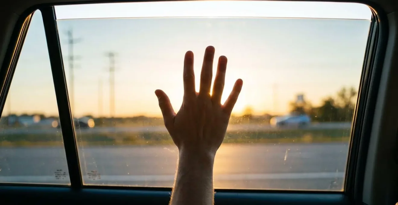 Silhouette d'une main levée en geste d'excuse visible à travers une vitre de voiture