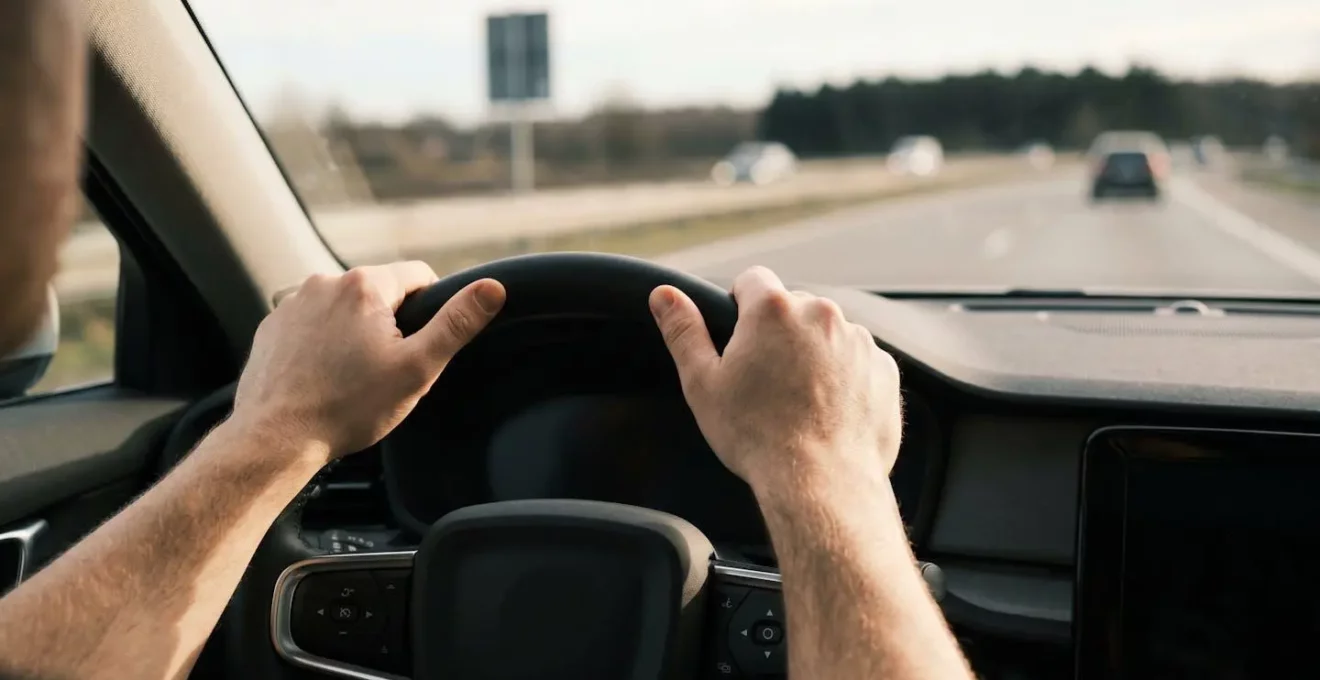 Mains d'un conducteur sur le volant avec point de repère visible au loin sur l'autoroute