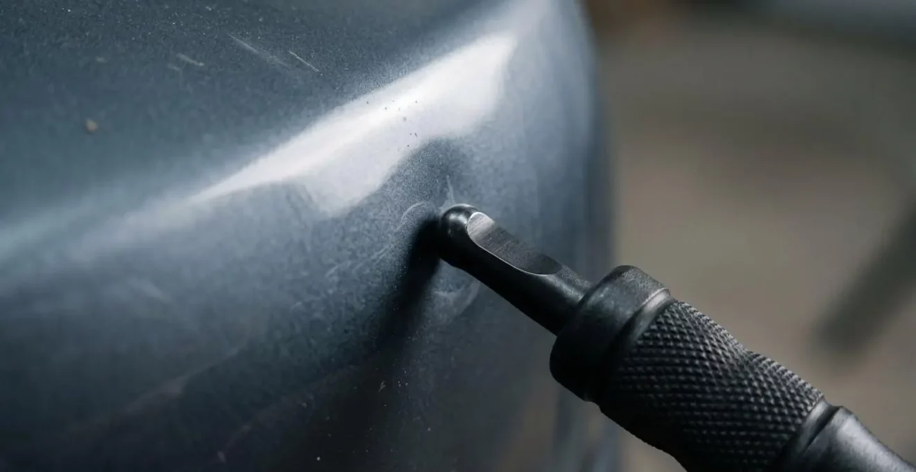 Gros plan sur une technique de débosselage sans peinture montrant des outils spécialisés et une surface métallique